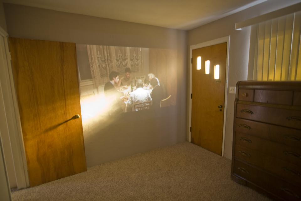 video projection of family dinner on wall in sunlit room