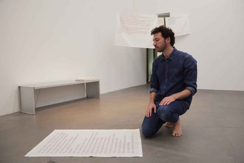 artist kneeling in front of fabric with text printed on it and speaking